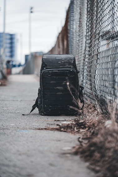 Close-up of a sleek, black Urbancarry backpack resting on a city bench with blurred urban skyline in the background.