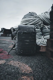 A rugged all-purpose sports bag resting on a rocky shoreline beside fishing gear.