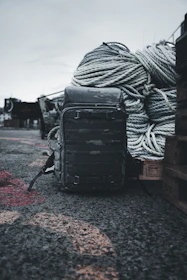A rugged all-purpose sports bag resting on a rocky shoreline beside fishing gear.