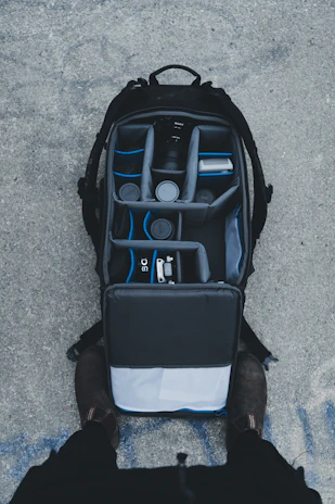 A compact backpack open to reveal organized compartments with video recording accessories.
