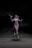 A statue or figure of a mystical woman with flowing garments, colored in shades of gray and purple. She stands with arms outstretched, holding a small bird in her right hand. The background is dark, adding a dramatic contrast to the figure.