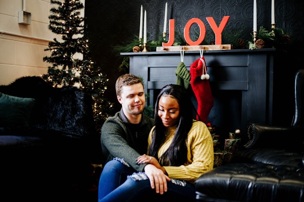 A happy couple wearing colorful monee llc slippers, sitting by a fireplace with smiles.