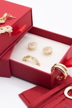 A bright, elegant jewelry box open to reveal sparkling earrings and a delicate necklace on a soft white background.