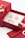 A red jewelry box contains ornate golden earrings and a ring. The box is open, revealing a white interior that highlights the jewelry. There are additional golden rings placed nearby, adding to the luxurious display.