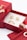 A red jewelry box contains ornate golden earrings and a ring. The box is open, revealing a white interior that highlights the jewelry. There are additional golden rings placed nearby, adding to the luxurious display.