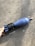 A hand is visible holding a blue mortar shell with visible markings on its body. The object rests on a rough, textured surface that appears to be concrete.