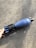 A hand is visible holding a blue mortar shell with visible markings on its body. The object rests on a rough, textured surface that appears to be concrete.