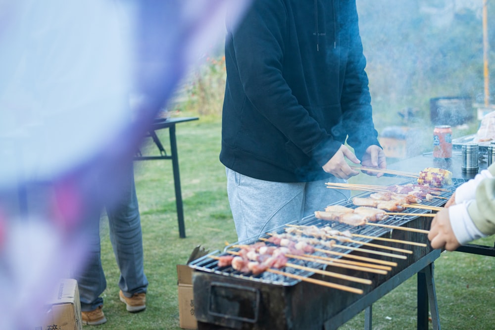 a group of people standing around a grill with food on it