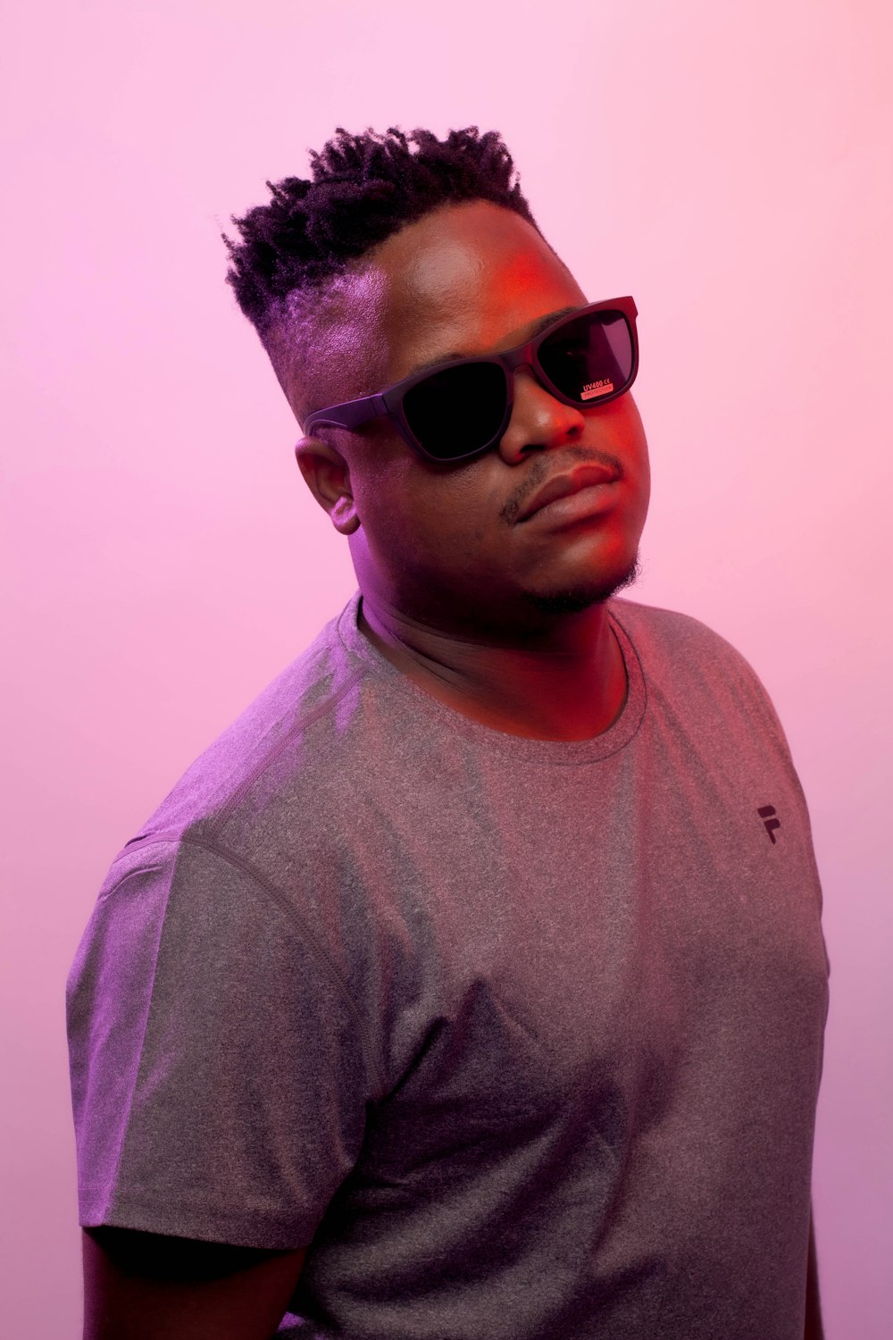 a man wearing sunglasses standing in front of a pink background