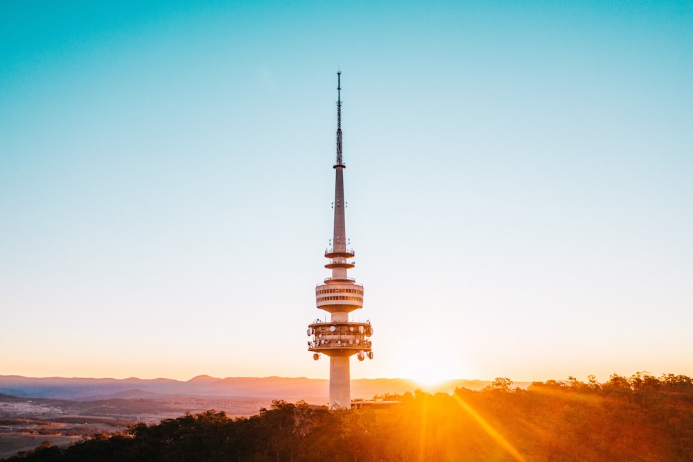 o sol está se pondo atrás de uma torre no topo de uma colina