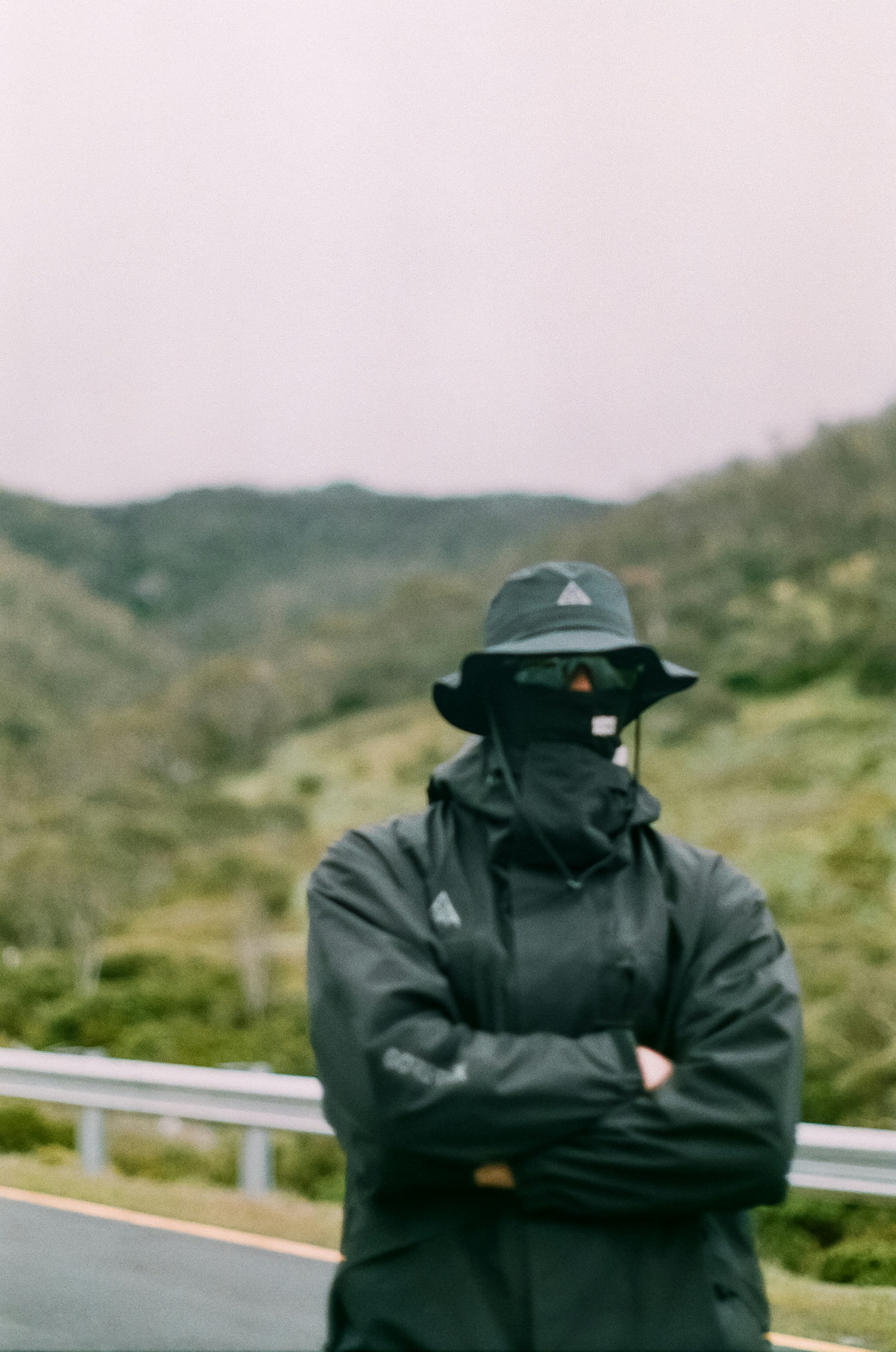 a man in a black jacket and hat standing on the side of a road