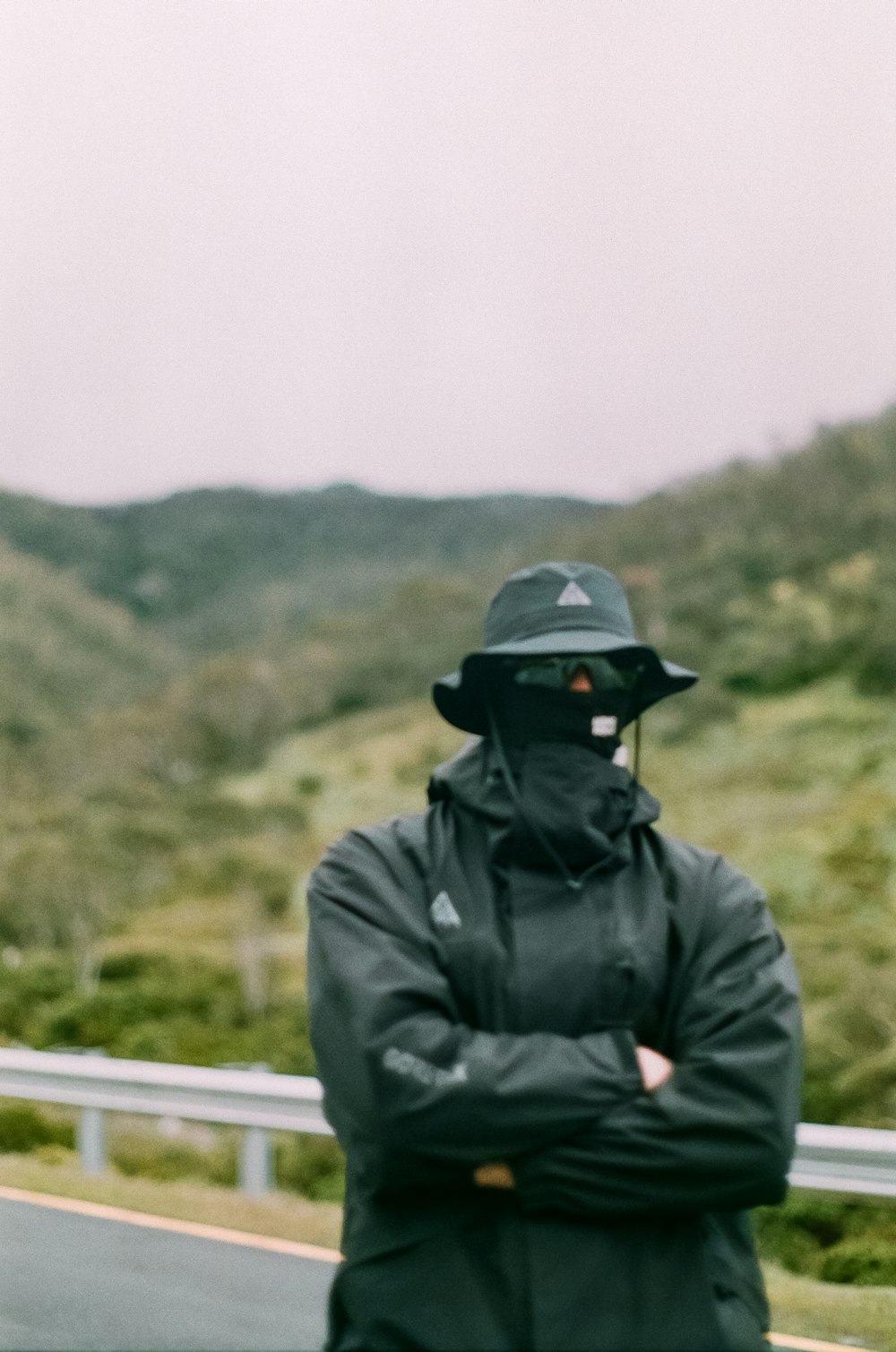 a man in a black jacket and hat standing on the side of a road