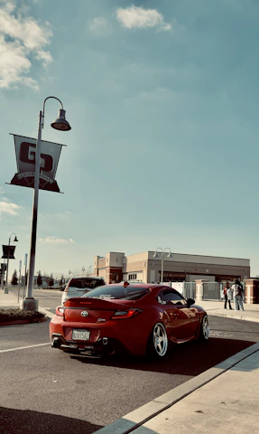 A sleek red car parked near India Gate under a clear blue sky.