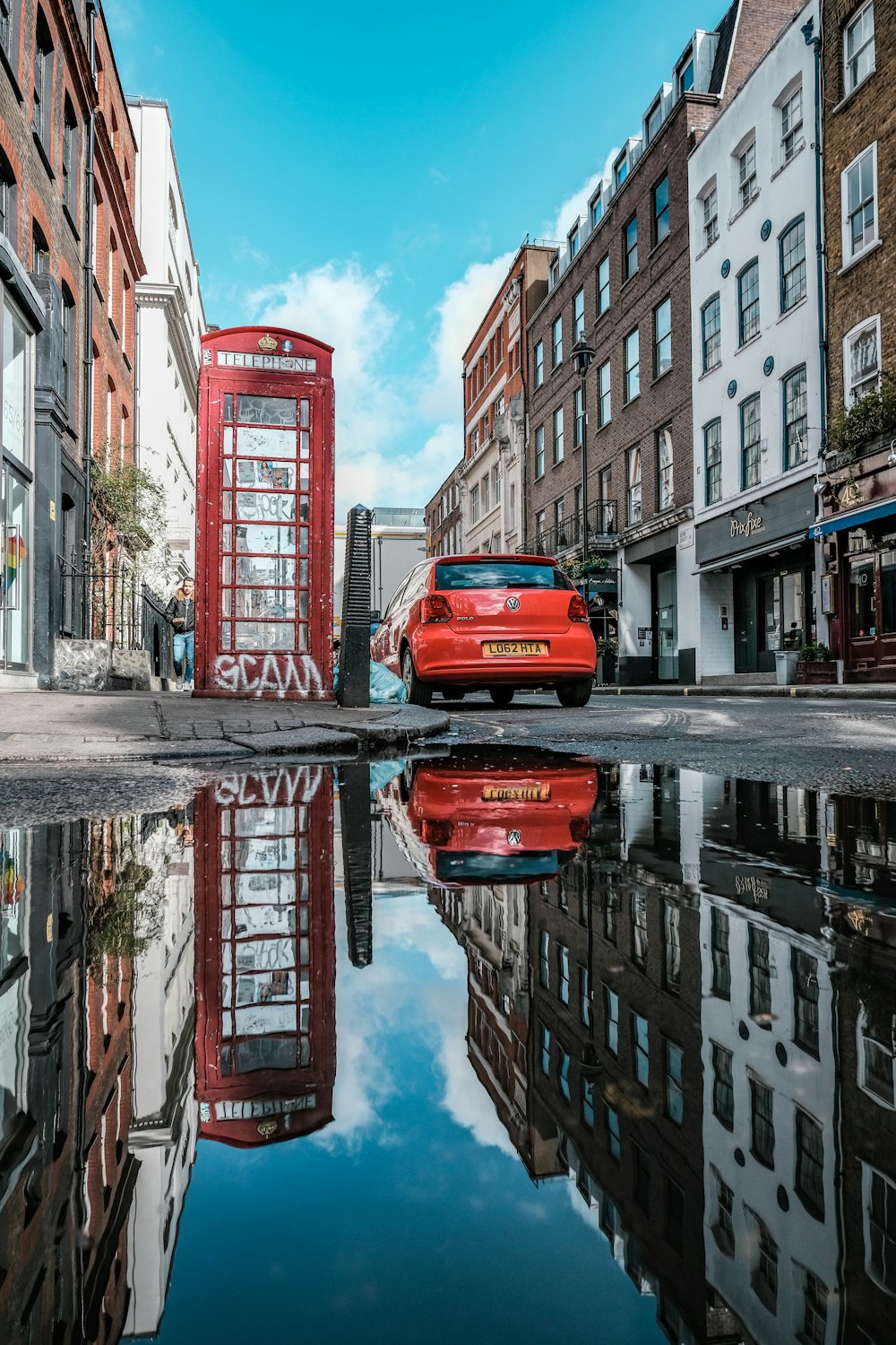 a red car parked in front of a red phone booth