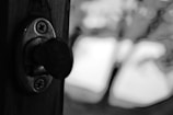 A black and white close-up of a keyhole in a door with a visible key inserted. The background is blurred, providing an abstract and artistic feel.