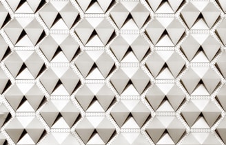 A geometric pattern composed of repeated three-dimensional pyramid-like shapes, each enclosed in a hexagon. The design features a structured and uniform arrangement, with subtle shading creating a sense of depth.