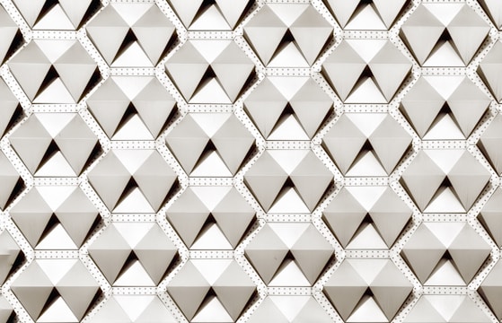 A geometric pattern composed of repeated three-dimensional pyramid-like shapes, each enclosed in a hexagon. The design features a structured and uniform arrangement, with subtle shading creating a sense of depth.