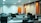 An empty office space with multiple workstations, each equipped with a computer monitor and office chairs. The room is well-lit with overhead fluorescent lights and features white and orange walls.