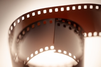 A close-up view of a curved, vintage film strip with perforated edges, illuminated from behind, creating a warm, nostalgic aura.
