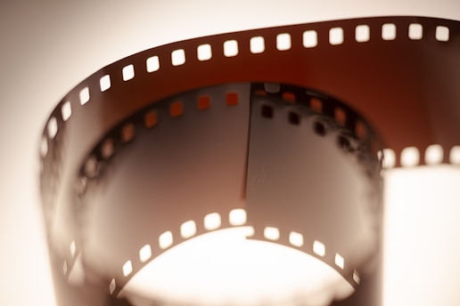 A close-up view of a curved, vintage film strip with perforated edges, illuminated from behind, creating a warm, nostalgic aura.