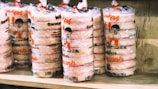 Several stacks of packaged edibles are displayed on a wooden shelf. The packaging has a clear plastic wrap with illustrations of a cartoon character and text in a bright orange color.