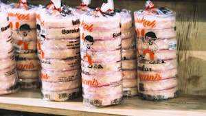 Several stacks of packaged edibles are displayed on a wooden shelf. The packaging has a clear plastic wrap with illustrations of a cartoon character and text in a bright orange color.
