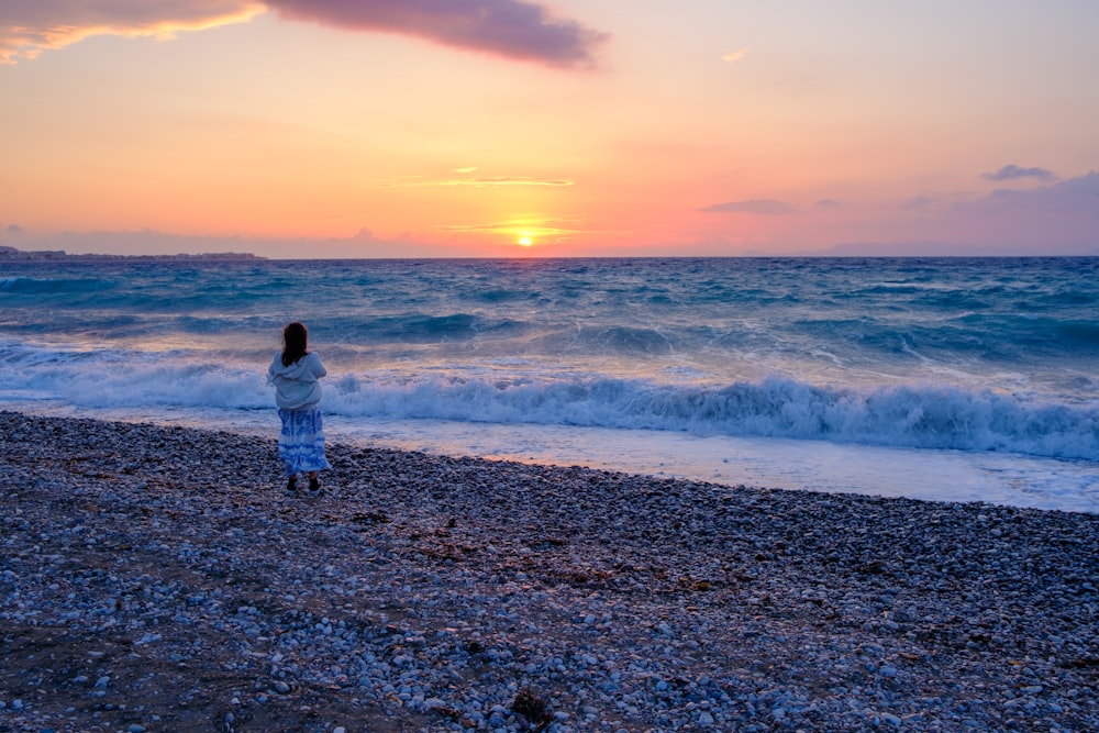 a woman standing on top of a beach next to the ocean