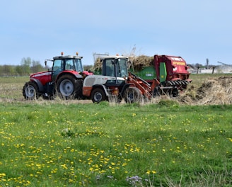 a red tractor pulling a trailer of hay through a field