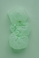 Three tied green plastic garbage bags are stacked vertically against a similarly colored green background, creating a monochromatic effect.