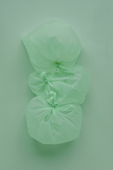 Three tied green plastic garbage bags are stacked vertically against a similarly colored green background, creating a monochromatic effect.