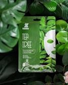 A fresh, green-themed container of acne remover cream with tea tree leaves in the background.