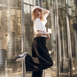 A sophisticated casualwear outfit styled with a fitted hat, captured in natural light against minimalist architecture.