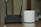 A black D-Link Wi-Fi router with two antennas is placed next to a white cylindrical Deco device on a wooden surface. The background appears to be a blurred indoor setting.