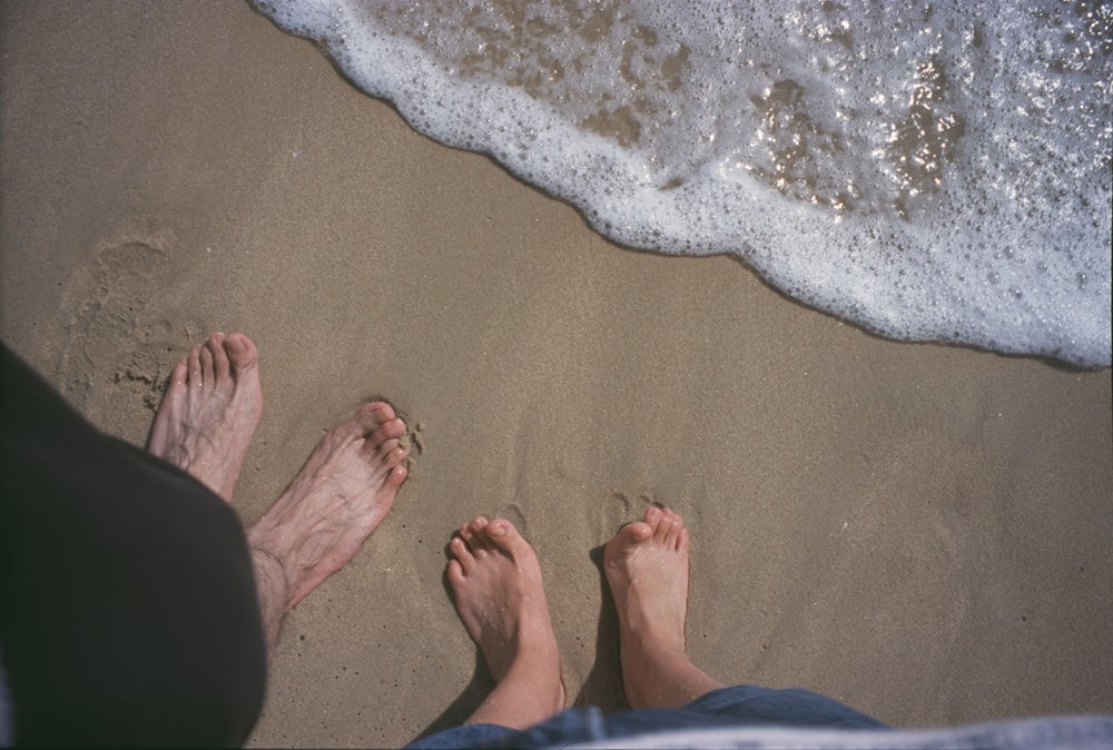 two people standing on a beach with their feet in the sand