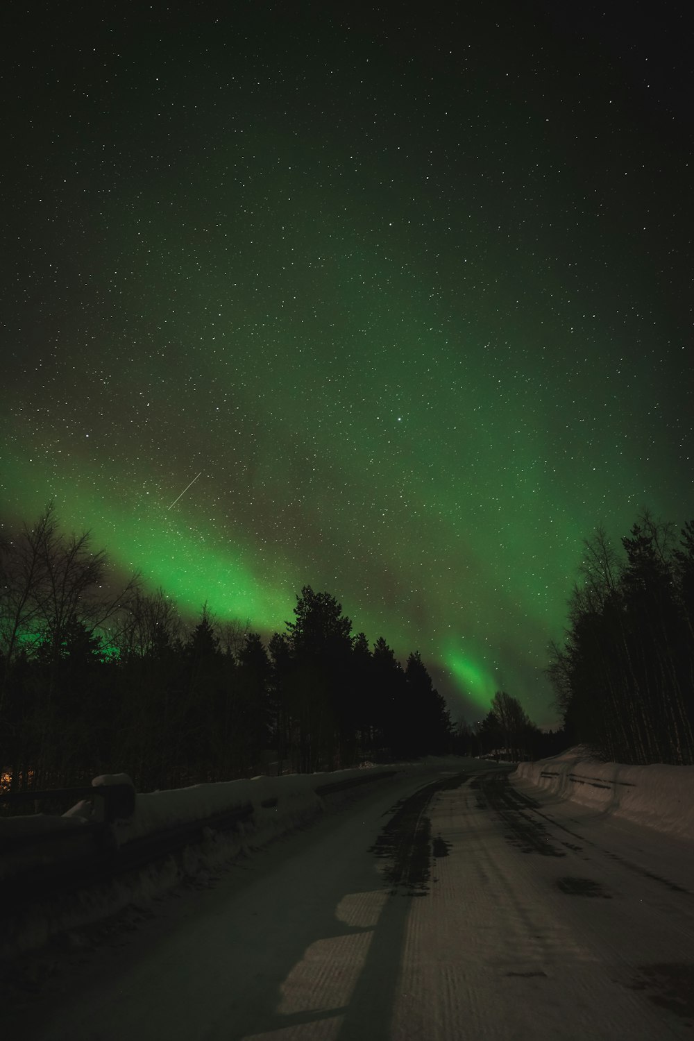 a road with snow on the ground and green lights in the sky