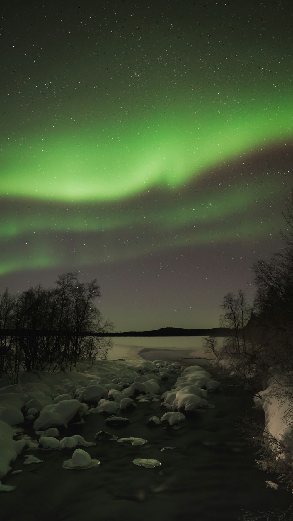 a green and white aurora over a frozen river