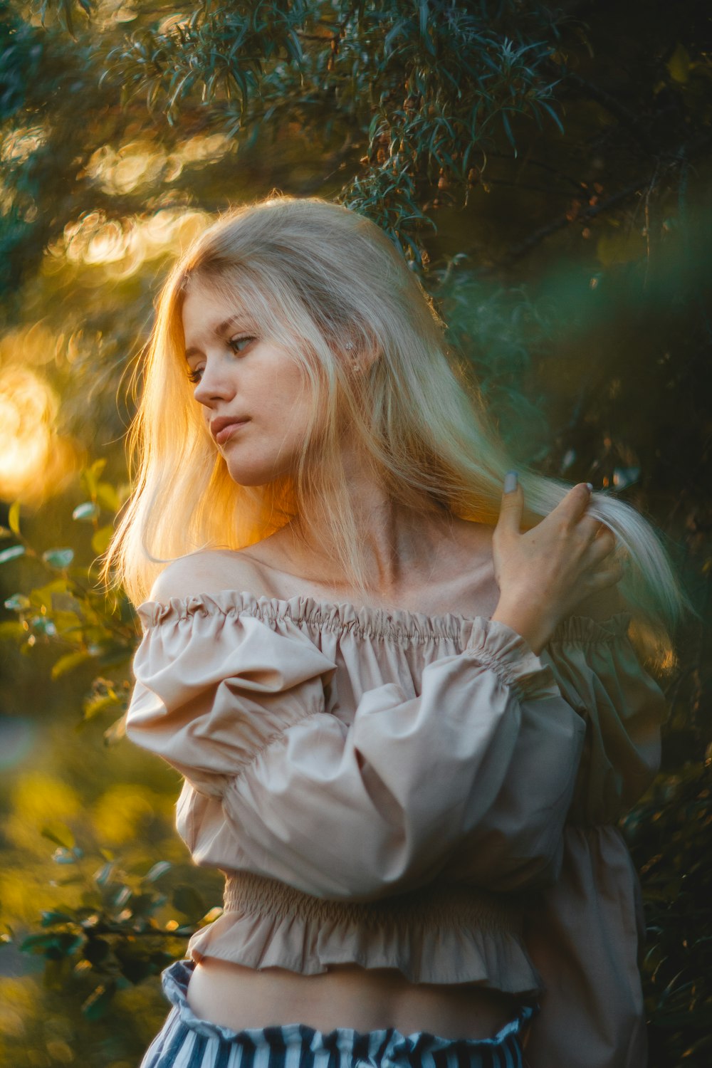 a woman with long blonde hair standing in front of a tree