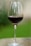A close-up of a wine glass filled with red wine, set against a blurred vineyard background.