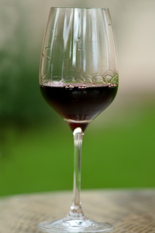 An elegant wine glass catching the light, filled with a deep red wine, resting on a wooden table.