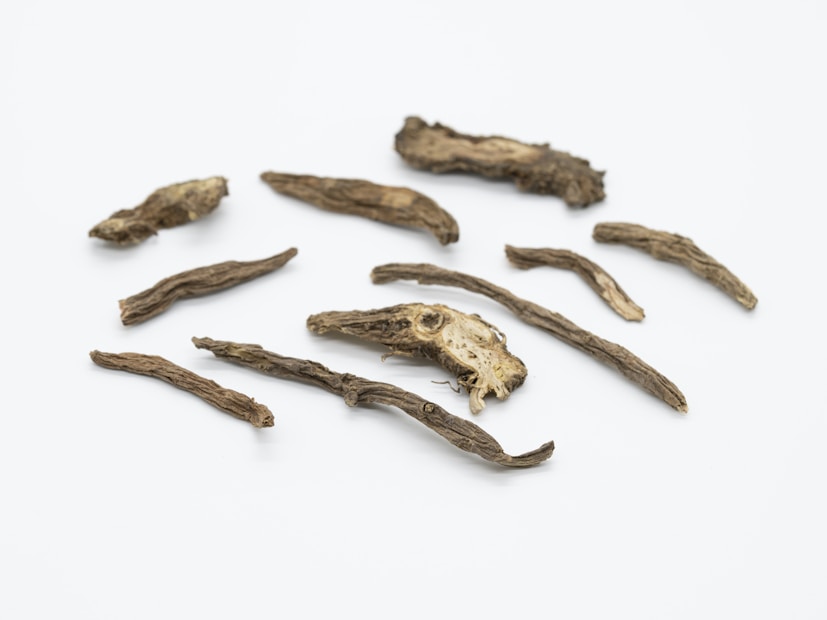Several pieces of dried roots and herbs are scattered on a plain white background. The texture of the roots appears rough and fibrous, with varying lengths and thicknesses.