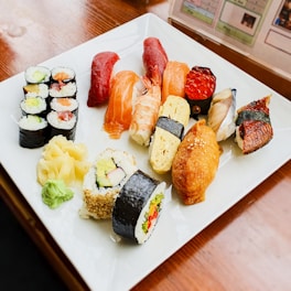 An assortment of non-vegetarian sushi including lamb vindaloo and hyderabadi dum biryani sushi on a slate platter.