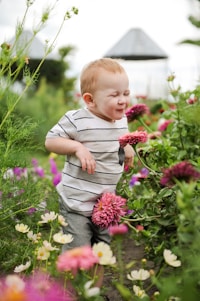 A joyful child wearing a vibrant bow and necklace, smiling in a sunny garden.