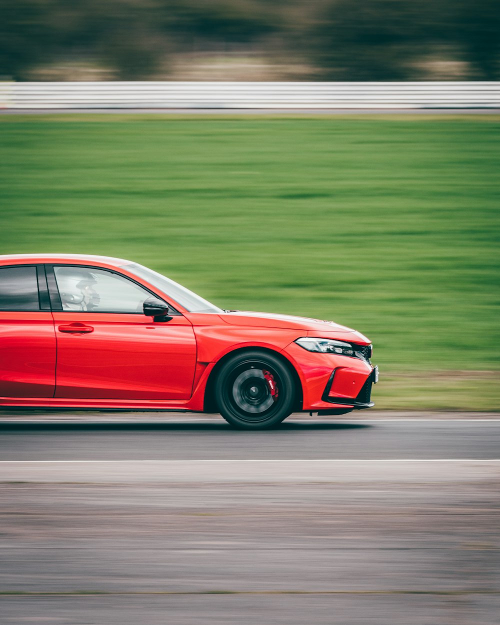 a red car driving down a road next to a lush green field