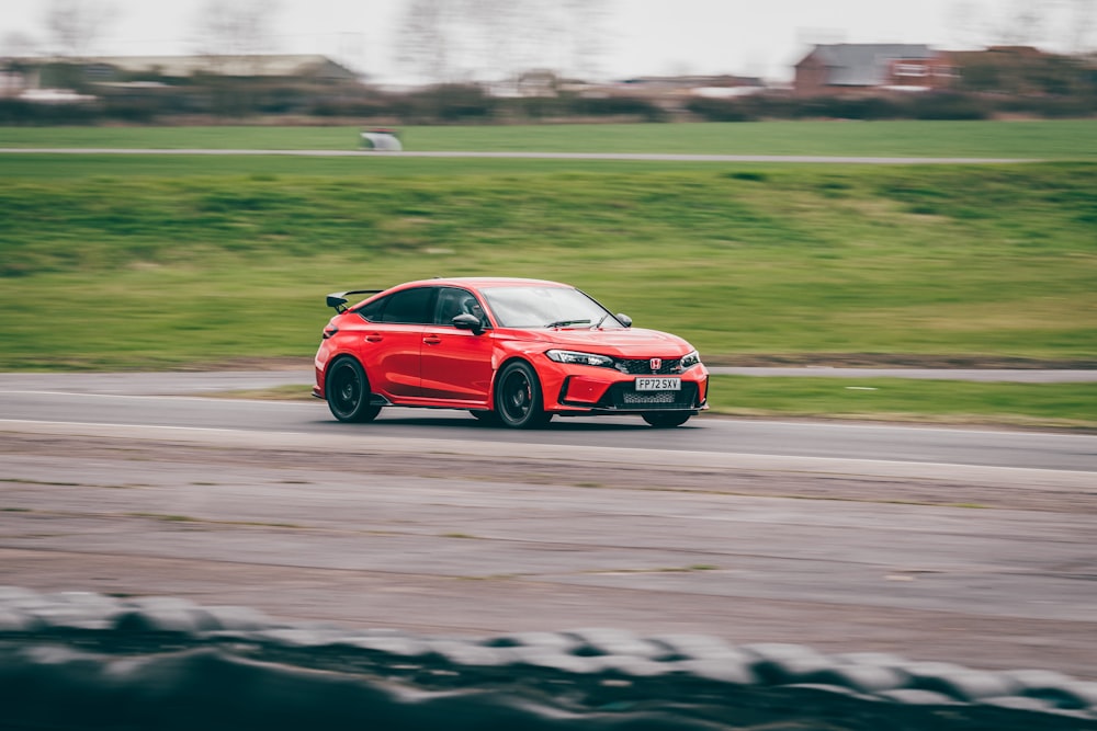 a red car driving down a road next to a lush green field