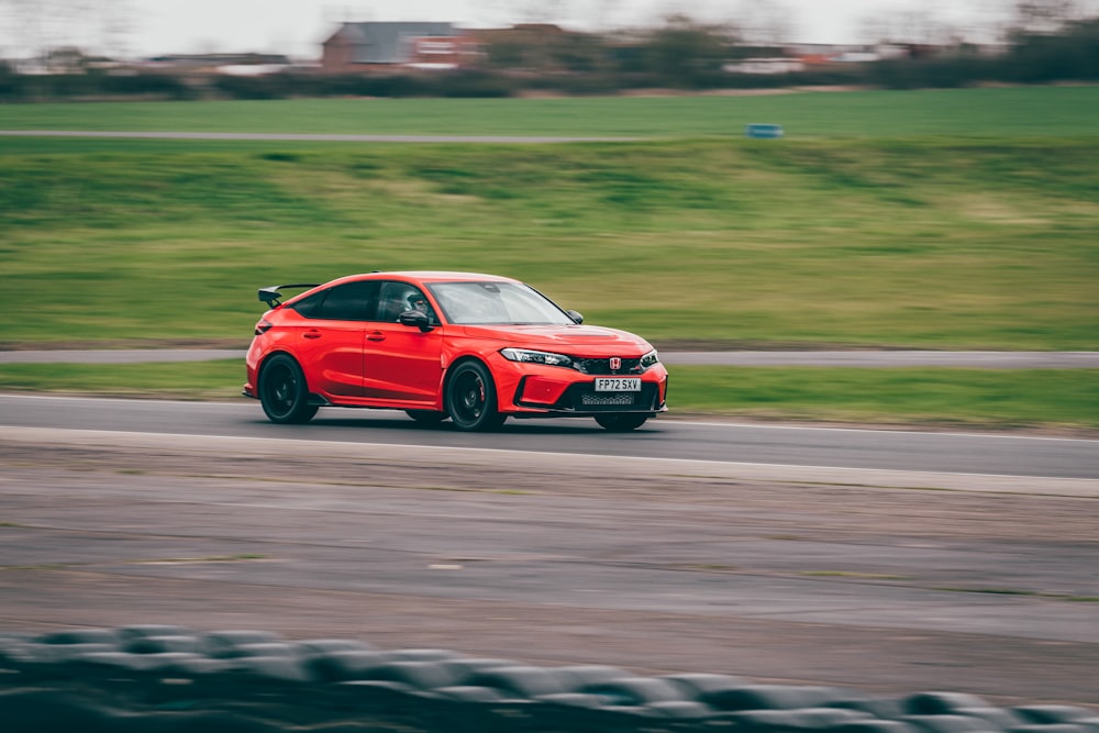 a red car driving down a road next to a lush green field