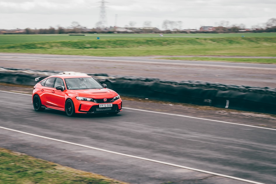 a red car driving down a road next to a field