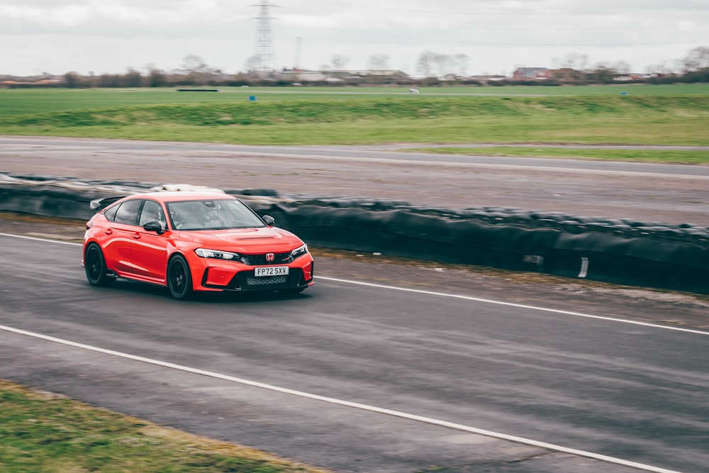 a red car driving down a road next to a field