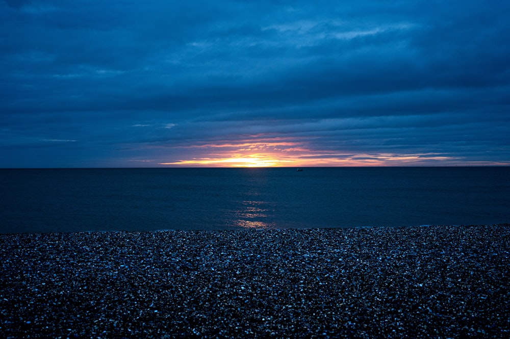 the sun is setting over the ocean on a cloudy day