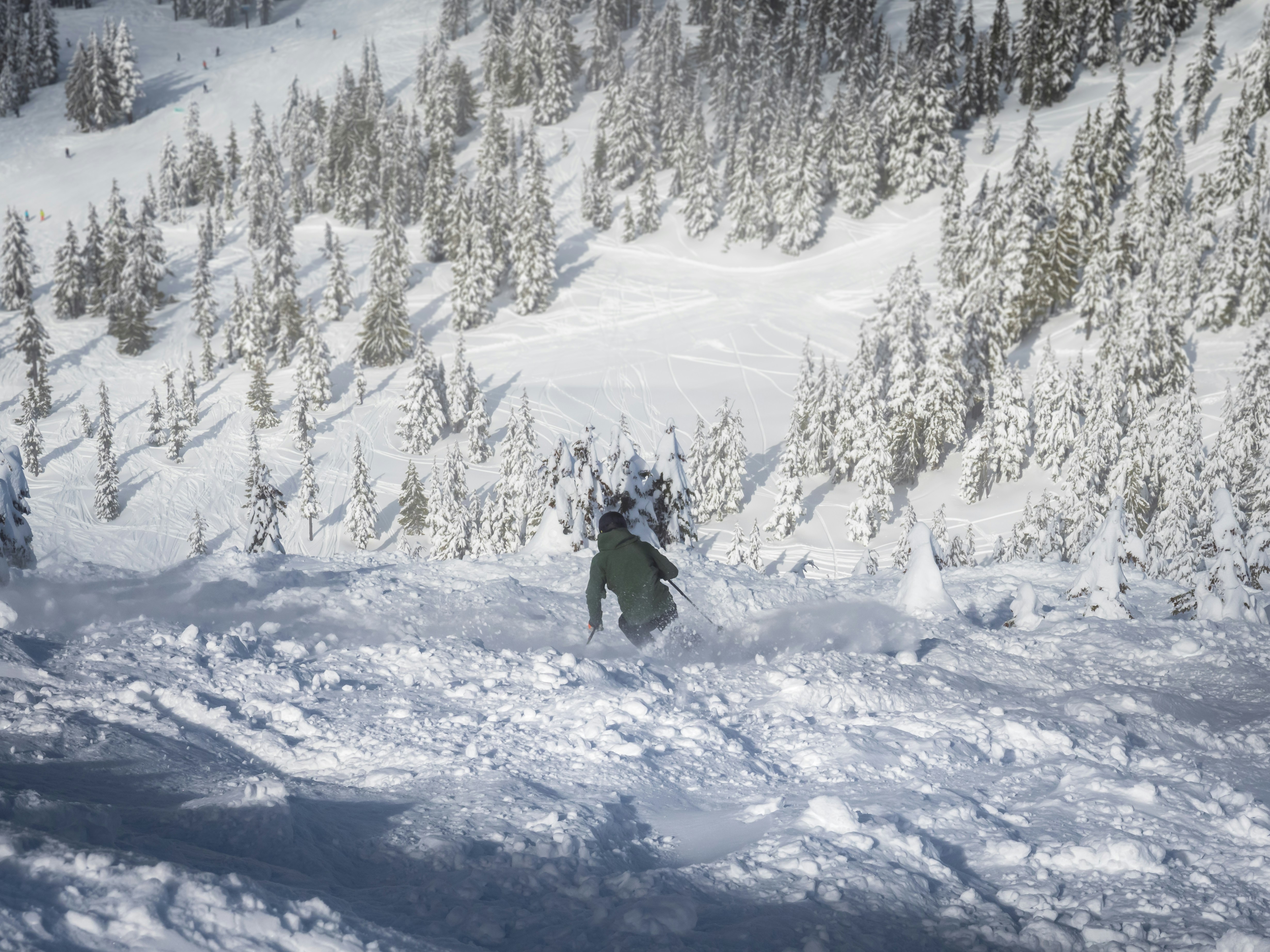 a man riding a snowboard down a snow covered slope, skier on a steep run with small trees in the distance