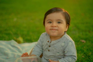 a baby sitting in the grass with a plastic container